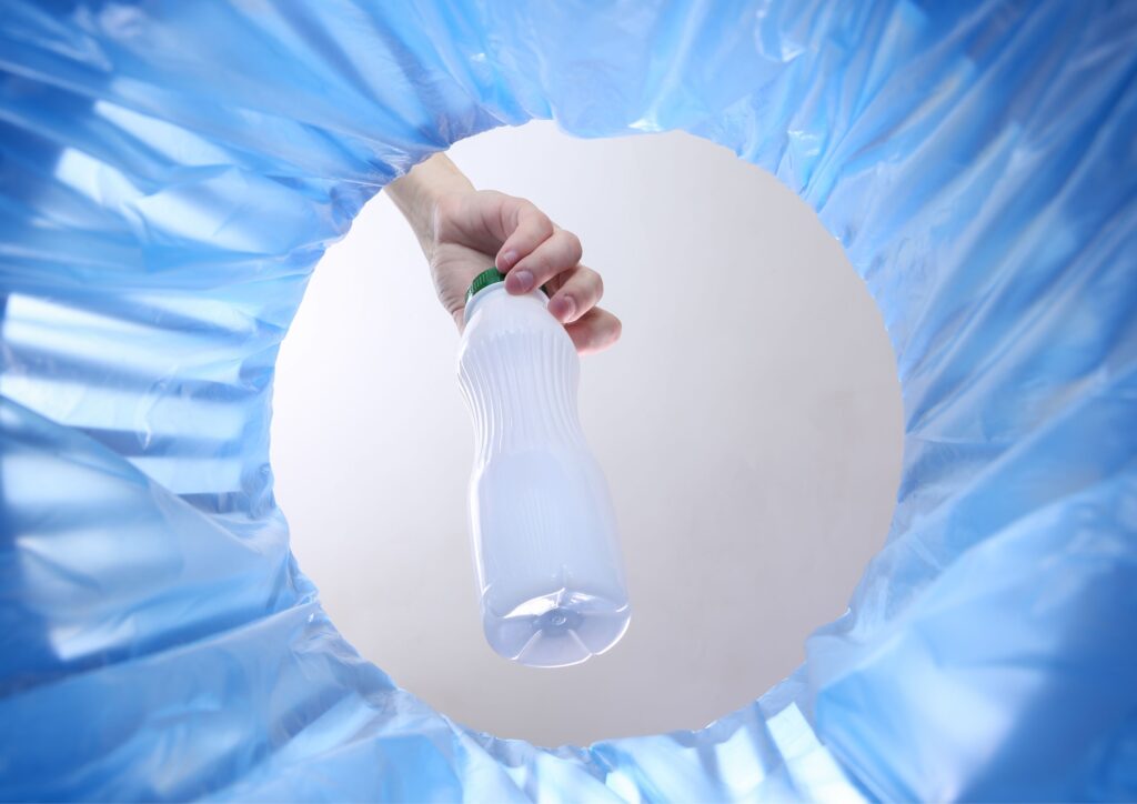 ręka wyrzucająca plastikową butelkę do kosza